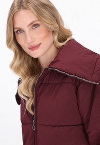 Giacca a vento bordeaux con colletto alto, texture trapuntata e dettagli sullo zip in argento. Caratterizzata da una silhouette aderente e materiale leggero.