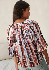 Multicolor Batikbluse mit Puffärmeln, einer gerafften Rückenpasse und einem weichen, leichten Stoff in Rot-, Blau- und Cremetönen.