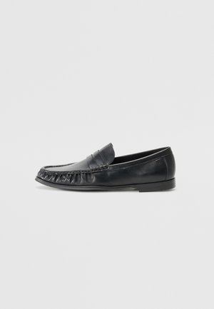 Mocasín negro de cuero tipo penny loafer con costura moc toe y tacón bajo, mostrado en perfil lateral izquierdo sobre fondo liso.