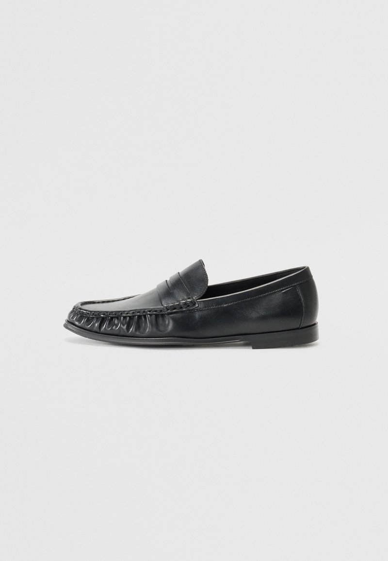 Mocassin penny loafer en cuir noir avec coutures moc toe et petit talon, présenté en profil gauche sur fond uni.