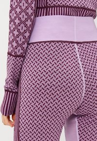 Conjunto de athleisure texturizado en púrpura y lila con patrones geométricos y acentos acanalados, con un diseño ajustado y cintura elástica.