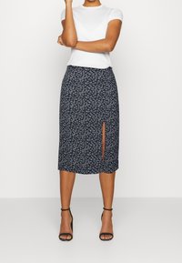 Marineblumenkleid Midi mit seitlichem Schlitz und einem dezenten weißen Blumenmuster. Hergestellt aus leichtem Gewebe mit geradem Schnitt.