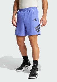 Pantalones cortos deportivos de color púrpura claro con una cinturilla elástica. Presenta tres acentos de rayas negras en el costado. Combinados con zapatos y calcetines negros.