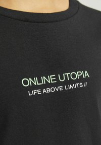 Melna kokvilnas T-krekls ar zaļu drukātu tekstu: "ONLINE UTOPIA" un "LIFE ABOVE LIMITS //". Riepas kakla dizains, gluda tekstūra.