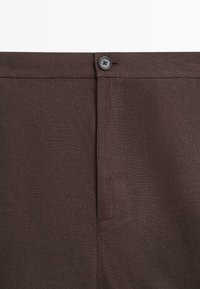Dark brown fabric trousers close-up showing waistband with a button and fly closure.