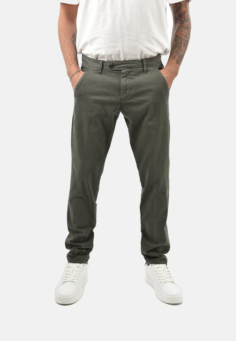 Chinos verdi in cotone con taglio dritto, chiusura con bottone, tasche laterali e una texture liscia, abbinati a sneaker bianche.