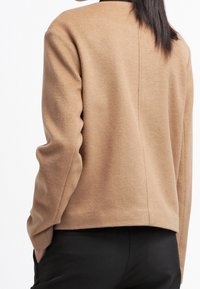 Brązowy wełniany sweter o luźnym kroju, z długimi rękawami, wysokim kołnierzem i gładką fakturą, przedstawiony z tyłu.