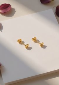 Orecchini a forma di cuore in oro con finitura lucida, posati su uno sfondo bianco, accompagnati da petali di rosa sparsi.