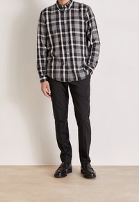 Koszula zapinana na guziki w czarno-szary wzór kratki, z długimi rękawami zakończonymi mankietami. Połączona z czarnymi spodniami i czarnymi butami. Prosty, dopasowany fason.