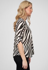 Black and white zebra print top with three-quarter sleeves, featuring rolled cuffs and a loose fit, made from lightweight fabric.