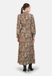 Robe maxi à imprimé léopard beige, avec des manches longues et une taille ceinturée. Présente un tissu doux, un col haut, et une coupe longue jusqu'aux chevilles. Portée avec des bottines noires.