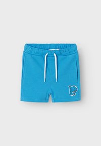 Blaue Shorts aus weichem Stoff, mit einem elastischen Bund und weißem Kordelzug sowie einem Haifischgrafik auf dem linken Oberschenkel.