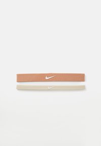 Dva tkanina elastična trakica za kosu: jedna u terakotna boji s bijelim Nike logom, a druga u bež boji. Obe imaju glatku teksturu i fleksibilan dizajn.