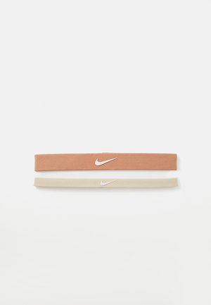 Dva tkanina elastična trakica za kosu: jedna u terakotna boji s bijelim Nike logom, a druga u bež boji. Obe imaju glatku teksturu i fleksibilan dizajn.