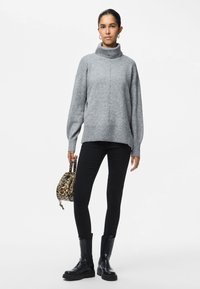 Pilkas megztas golfo stiliumi džemperis su nuleistais pečiais ir banguota apatine dalimi, derinamas su juodais siaurais džinsais ir juodais auliniais batais. Laiko leopardų rašto rankinę.