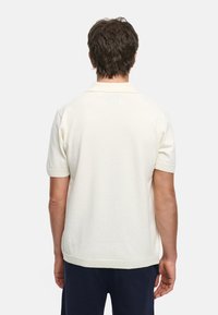 Kremfarget kortermet polo-skjorte med teksturert stoff og ribbestrikkede mansjetter, med klassisk krage og avslappet passform.