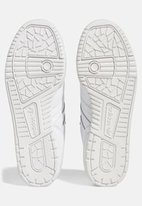 Vita sportskor i vitt med strukturerade gummisulor, med tre svarta ränder och en cirkulär detalj nära hälen.