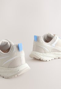 Baltas acs sporta apavi ar ziliem akcentiem, teksturētām sintētiskām pārklājumiem un raibām zolēm. Aprīkoti ar aizmugures cilpu ērtai uzvilkšanai.