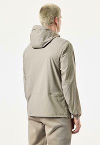 Lightweight, beige waterproof jacket with a hood, elastic cuffs, and side pockets. Smooth texture, minimalistic design, and streamlined shape.