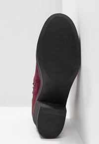 Semelle d'une botte en daim marron avec semelle en caoutchouc noire et petit talon, taille 37 visible, positionnée debout contre un fond blanc d'angle.