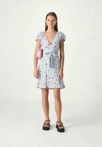 Rochie florală de un albastru deschis, cu un decolteu în V, mâneci bufante și cu un legat în față. Asortată cu o geantă mică roz și sandale cu bretele negre.