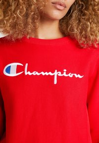 Rode sweatshirt van katoen met ribbelboord. Beschikt over een witte geborduurde "Champion" logo met blauwe accenten. Standaard pasvorm, gladde textuur.