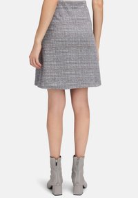 Grijze geruite A-lijn rok van een gestructureerde tricot, met een lengte tot halverwege de dij. Gecombineerd met lichtgrijze enkelbootjes met een ritsdetail.