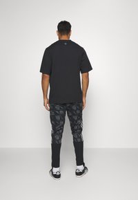 T-shirt noir à manches courtes associé à un jogging noir à motifs avec trois rayures blanches et des chaussures de sport noires.