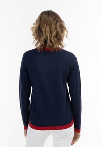 Pulover albastru cu mâneci lungi, accente roșii la guler și la tiv, realizat dintr-un material moale, cu un design ajustat, textură ribbed vizibilă.