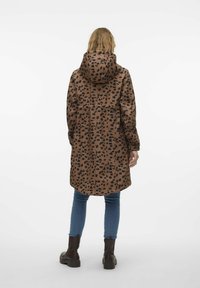 Brun leopardmönstrad regnjacka med huva, långa ärmar och en något avsmalnande form. Bärs över blå jeans och bruna stövlar.