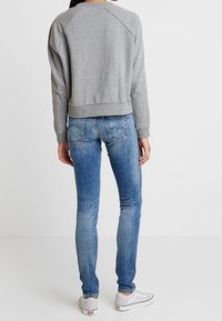Sudadera gris con puños y dobladillo acanalados, combinada con jeans skinny azules y zapatillas blancas. El conjunto presenta un diseño de corte relajado.