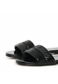 Sandales noires à glissière avec deux sangles texturées et striées et une semelle lisse. Le design met en valeur une esthétique minimaliste.