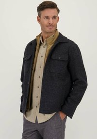 Navy wollen mix jacket met een knoopsluiting aan de voorkant, twee borstzakken en een contrasterende tan binnenvoering, gecombineerd met een lichtbeige shirt.