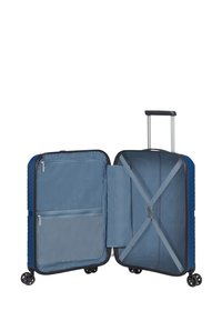 Valigia a mano rigida di colore blu con superficie testurizzata, doppie compartimenti, cinghie incrociate e numerose tasche interne.