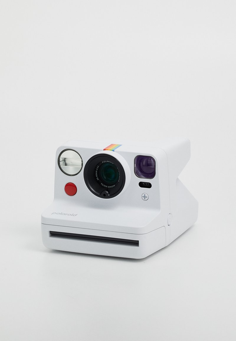 Appareil photo instantané Polaroid en blanc avec un boîtier arrondi, un objectif noir, un viseur circulaire, un bouton rouge et une bande arc-en-ciel.