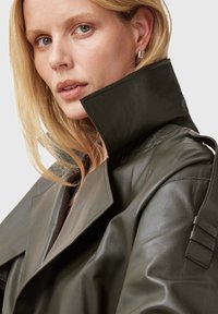 Trench coat in pelle verde scuro con colletto alto, caratterizzato da rever pronunciati e una finitura testurizzata. Accentuato da un dettaglio con maniche a cintura.