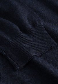 Zbliżenie na tkaninę ciemnogranatowego swetra, z prążkowanym mankietem, gładką teksturą i miękkim wzorem dzianiny, z subtelnymi wariacjami kolorów.