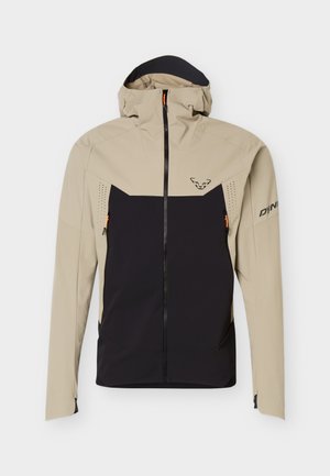 Béžovo-černá bunda s kapucí Dynafit s předním zipem, zipovanými kapsami na hrudi a logem na hrudi a levém rukávu.