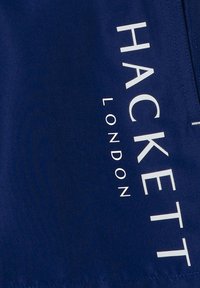 Námornícky modrú tkaninu s veľkým bielym textom "HACKETT" a "LONDON", hladká textúra, s čistým, minimalistickým dizajnom.