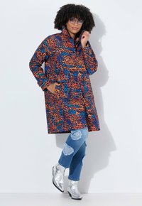 Multikleurige luipaardprintjas met een hoge kraag, zijzakken; gedragen over versleten blauwe jeans en zilveren enkellaarsjes.