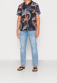 Czarna koszula z krótkim rękawem z żywymi wzorami pomarańczowego i niebieskiego smoka oraz tygrysa, zestawiona z jasnoniebieskimi dżinsami i czarnymi japonkami.