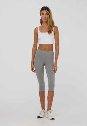 Top corto bianco con scollo quadrato abbinato a leggings grigi a tre quarti. Il modello indossa sneakers bianche e grigie.