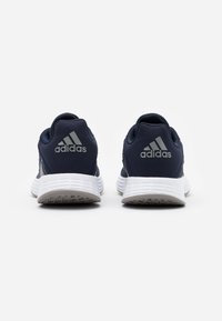 Ett par marinblå Adidas-sneakers visade från baksidan med vita strukturerade sulor och en framträdande Adidas-logotyp på hälfliken.