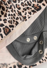 Leopard-patterned fabric in beige and black with light pink trim; features gray ribbed cotton at the bottom and metal snaps for closure.