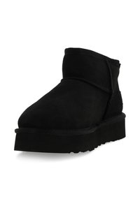 Stivaletto in suede nero con suola spessa, punta rotonda e cuciture visibili attorno alla parte superiore e alle aree del tallone.