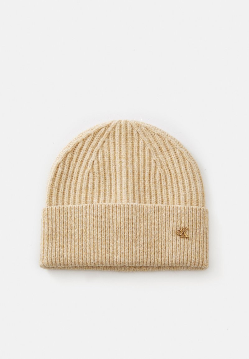 Tricot beanie in lichtbeige met verticale ribbels, een opgerolde boord en een klein gouden "CK" logo aan de voorkant. Zachte textuur, casual ontwerp.