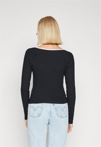 Zwarte geribbelde lange mouwen top met een brede witte hals, fitted design en gestructureerde stof, gecombineerd met lichtblauwe denim jeans.