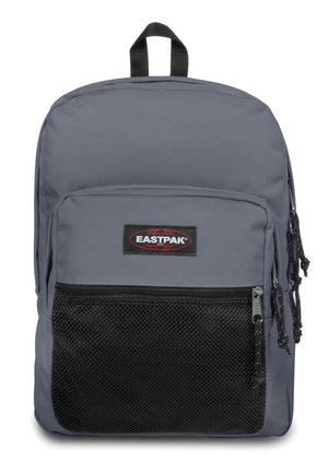 Zaino in tessuto grigio con tasca frontale in rete, manico superiore e cerniere. Presenta un'etichetta con logo nera e spallacci regolabili.