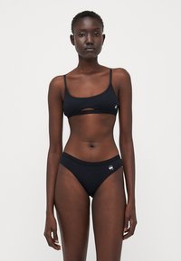 Fekete bikini rugalmas anyagból. Jellemzője egy cropped top elülső kivágással és hozzá illő, alacsony derekú alsó részek oldalsó logóval.