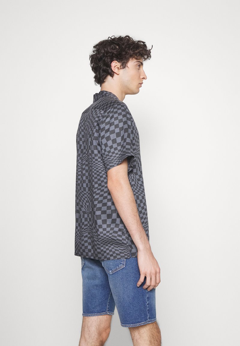 Camisa de cuadros de manga corta en negro y gris, que muestra un patrón geométrico. Combinada con pantalones cortos de mezclilla azul.